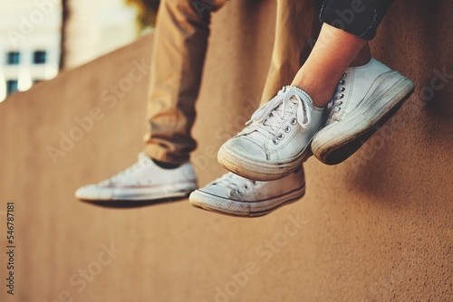 People, shoes and wall with friends relax outside by city building for bonding, fun and freedom. Carefree, footwear and urban building background with people together for casual friendship