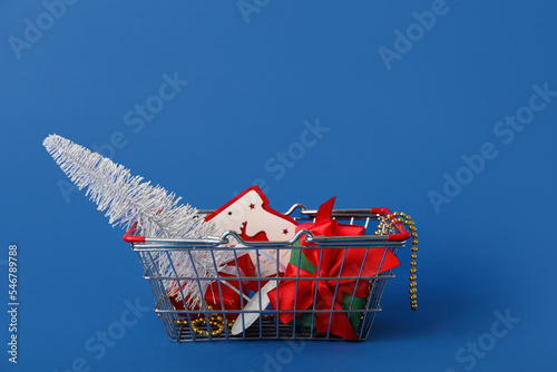 Shopping basket with Christmas tree, presents and beads on blue background