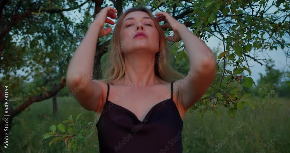 Romantic blonde girl, beautiful female blonde model acting on camera, straightens hair in the branches of an apple tree Romantic blonde girl, beautiful female blonde model acting on camera, straightens hair in the branches of an apple tree