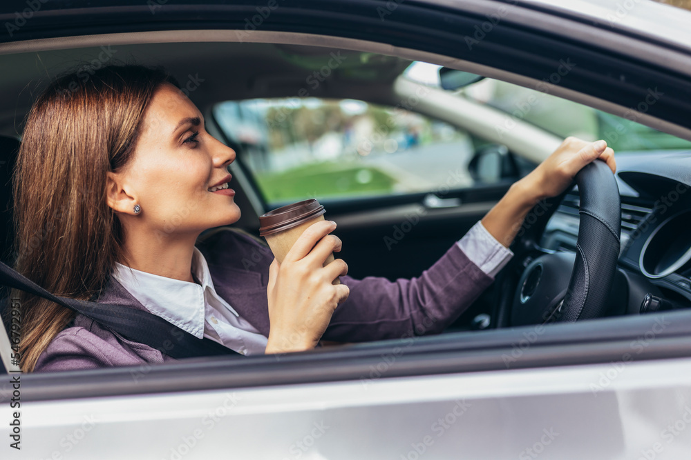 Young businesswoman driving in a car to work during the day, drink coffee. Steering wheel on the right side of the car