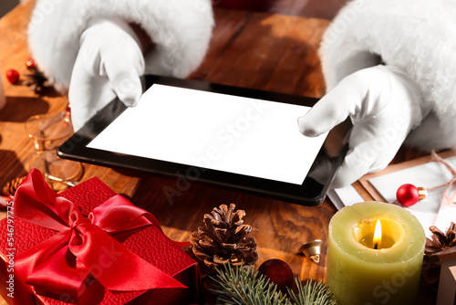 Santa Claus holding tablet computer on wooden table, closeup