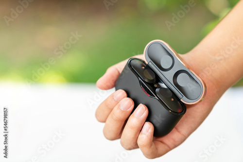 Black true wireless earphones in hand with charging case.