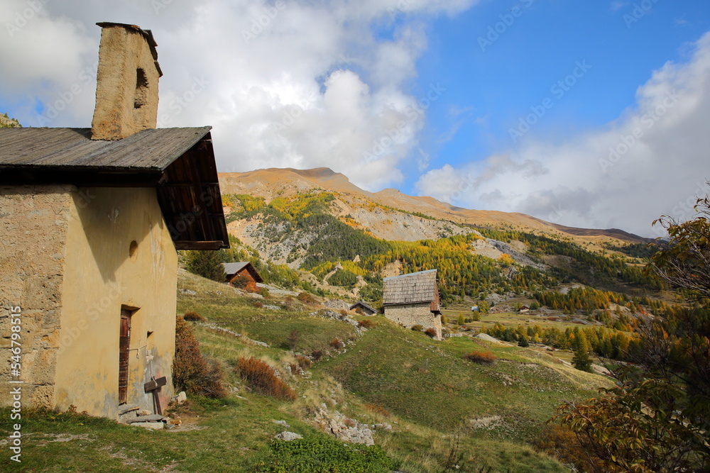 The hamlet Le Villard located along the Cristillan valley above Ceillac, Queyras Regional Natural Park, Southern Alps, France, with Sainte Barbe chapel, a traditional wooden chalet and Autumn colors
