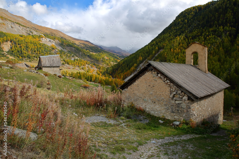 The hamlet Le Villard located along the Cristillan valley above Ceillac, Queyras Regional Natural Park, Southern Alps, France, with Sainte Barbe chapel, a traditional wooden chalet and Autumn colors