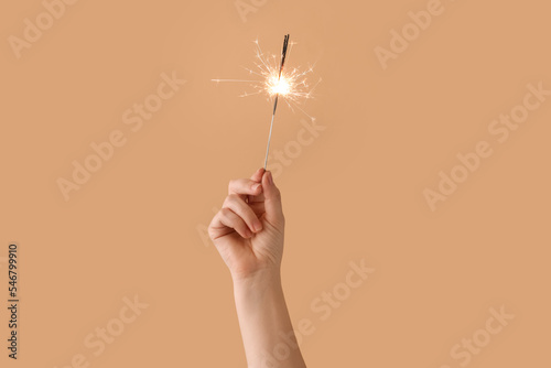 Female hand with burning Christmas sparkler on color background