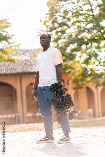 Giovane cameraman che utilizza una videocamera professionale per filmare notizie all'aperto con sfocatura dello sfondo. photo