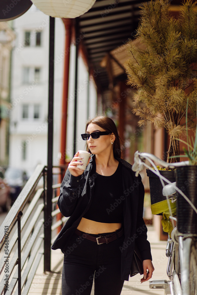 Fototapeta premium Outdoors lifestyle portrait of stunning brunette girl. Drinking coffee and walking on the city street.