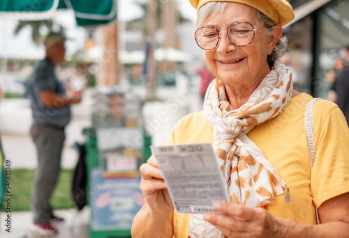 Bild auf Leinwand Smiling old woman checks if the lottery ticket was lucky