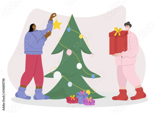 Two woman preparing for the new year, one of them decorating a Christmas tree for the holiday, hanging Christmas toys and the second puts gifts under the Christmas tree ,