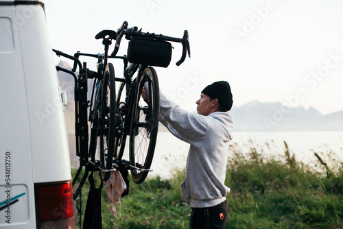 Foto Man attach two bikes to bike rack on back of camper van