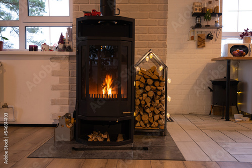 Black metal stove fireplace with wood in a woodpile - the interior of a private village house. Heating and heating of the house with firewood, the heat of the fire from the hearth. photo