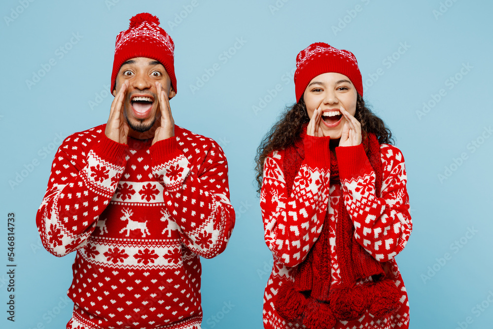 Merry young couple two man woman wear red Christmas sweater Santa hat posing scream hot news about sales hands near mouth isolated on plain pastel blue background Happy New Year 2023 holiday concept. Merry young couple two man woman wear red Christmas sweater Santa hat posing scream hot news about sales hands near mouth isolated on plain pastel blue background Happy New Year 2023 holiday concept.