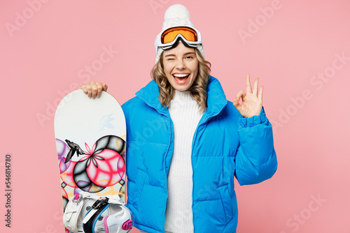 Snowboarder smiling happy cheerful woman wear blue suit goggles mask hat ski padded jacket show ok okay isolated on plain pastel pink background. Winter extreme sport hobby weekend trip relax concept.