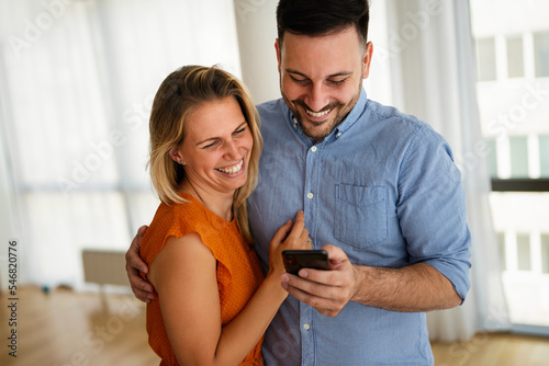 Smiling couple embracing while using a smartphone. People sharing social media on mobile phone.