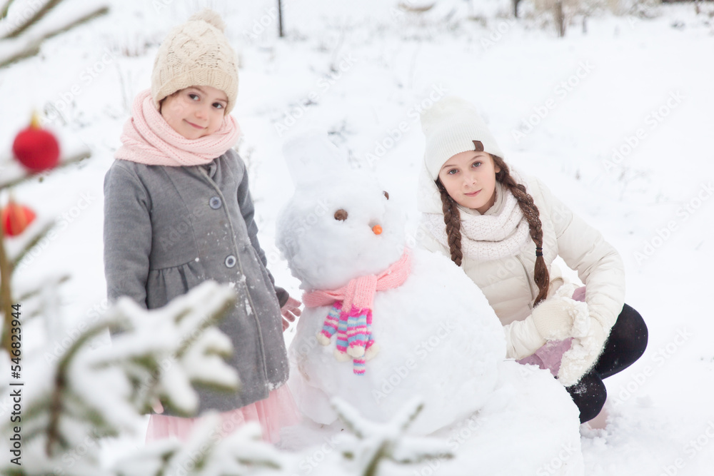 Sisters playing with a snowman with pink knitted scarf Sisters playing with a snowman with pink knitted scarf