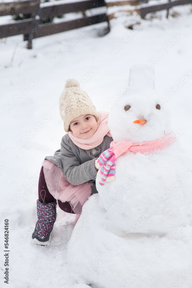 Girl playing with a snowman with pink knitted scarf