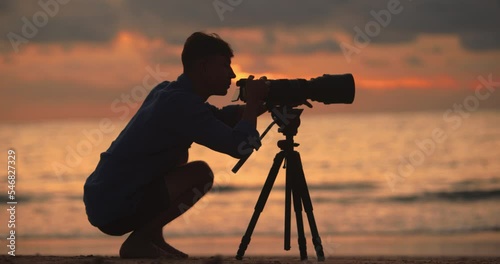 Silhouette of a man photographer with professional camera and long lens and tripod photographs a beautiful sunset 4K