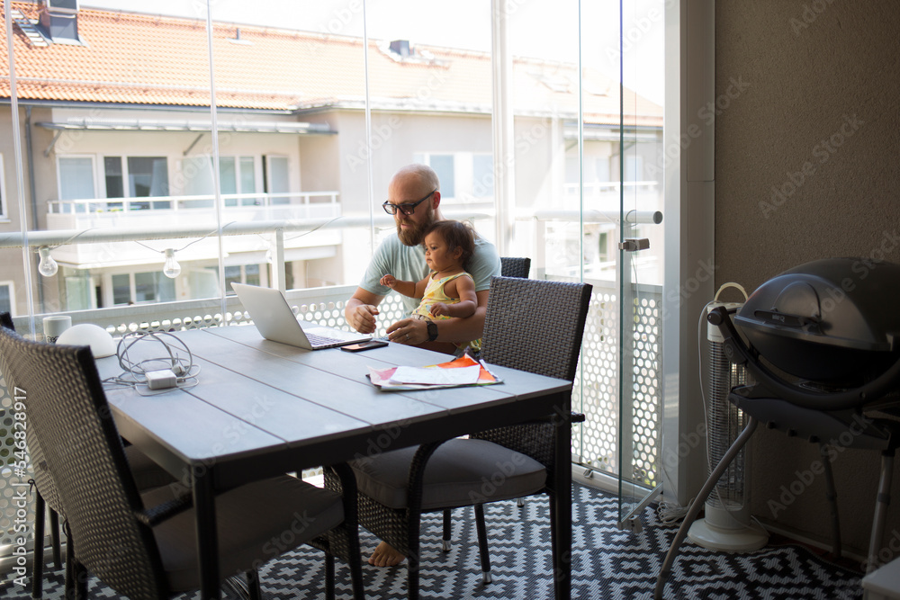 Man working from home while holding his daughter Man working from home while holding his daughter