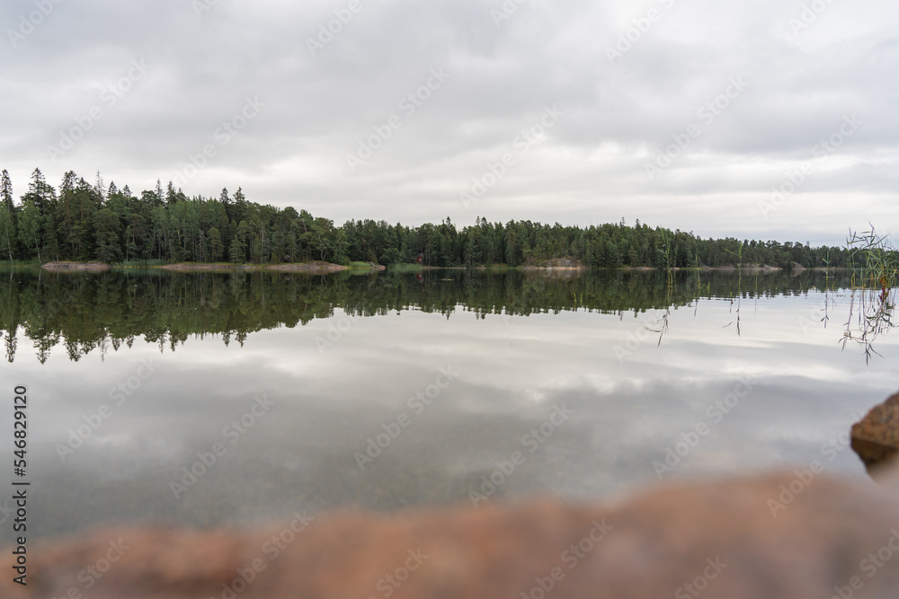 Beautiful view of the quiet lake reflecting the gray sky on a cloudy day outside. The rocky shore in the foreground is out of focus. Natural background.