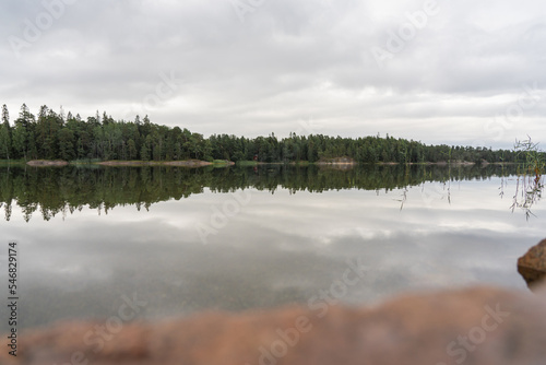Beautiful view of the quiet lake reflecting the gray sky on a cloudy day outside. The rocky shore in the foreground is out of focus. Natural background. © M.V.schiuma