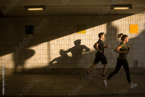 Young man and woman jogging by tiled wall
