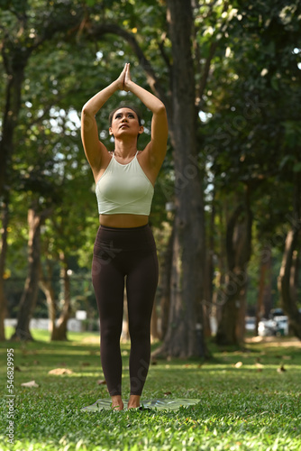 Full length portrait of sporty woman practicing yoga, standing in mountain with arms up pose in tropical garden
