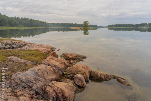 A small rocky island in the middle of a lake on a cloudy day. The rocky shore is in focus in the foreground. Autumn landscape. Natural background.