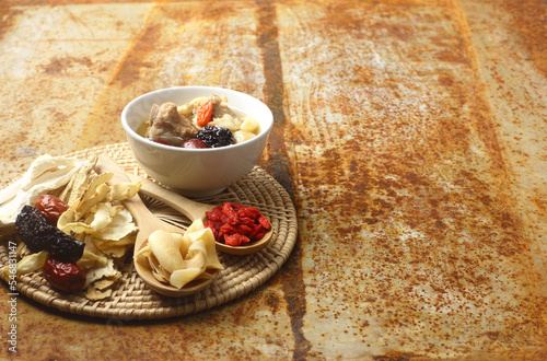 Chinese traditional nourishing healthy food - a white bowl of clear soup with Chinese herbal medicine - ginseng, gojiberry isolated on metal background.