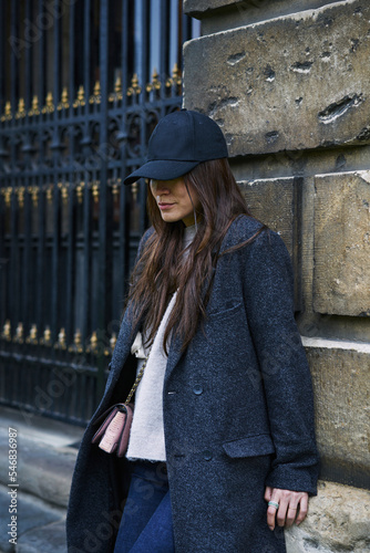 Woman in hat and coat leaning on wall