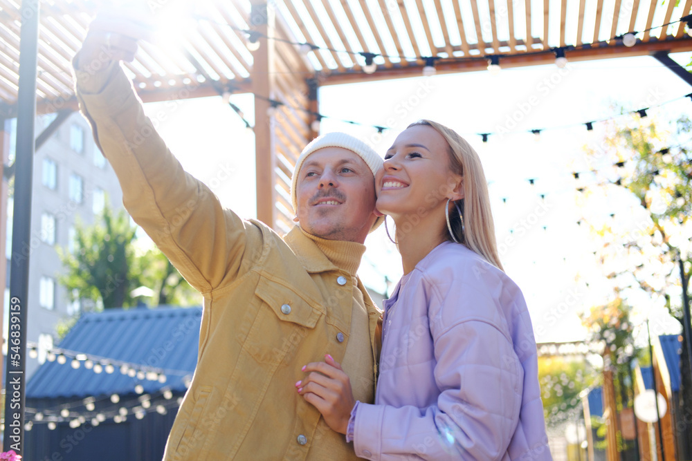 A couple in love, a guy and a girl, take a selfie together in sunny weather. couple looking at camera and smiling