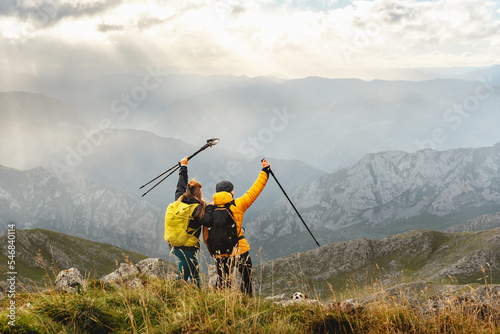 Couple of hikers with backpacks raising their trekking poles as they reach the top of a mountain. mountaineers contemplating the landscape of the mountain range. outdoor sports