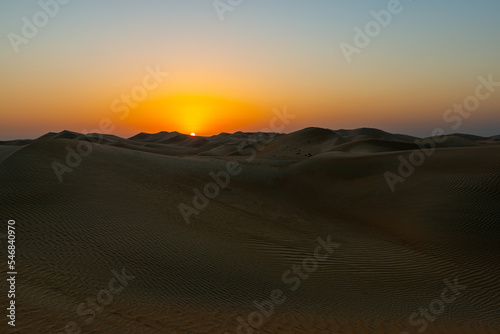 stunning and beautiful sunset over there wide and amazing desert with the sub setting over the dunes in the horizon 