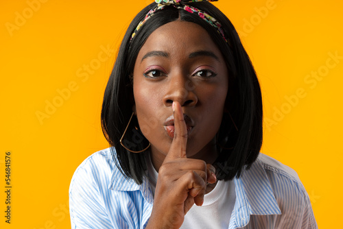 Young african woman asking to be quiet with finger on lips against yellow background photo