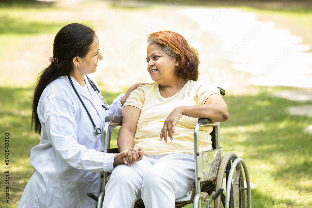 Obraz premium Indian caregiver nurse taking care and talking to senior female patient in a wheelchair outdoor at park, Asian doctor help and support elderly mature older people. rehabilitation and health care.
