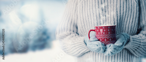 Fotografie, Tablou woman in wool sweater and mitten gloves holding a cup of hot steaming drink on snowy winter landscape background