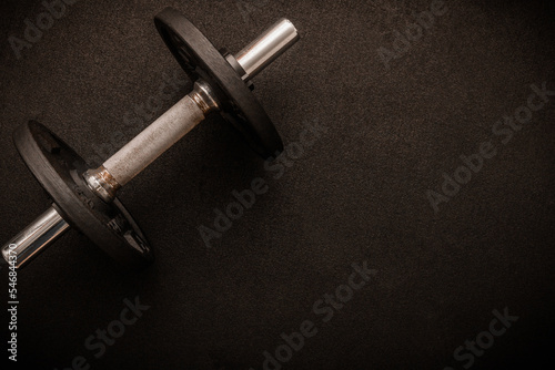 Loadable dumbbell on the floor at the gym. Top down view flat lay with bodybuilding equipment on a black background and empty space for text. Fitness, weight training or healthy lifestyle concept