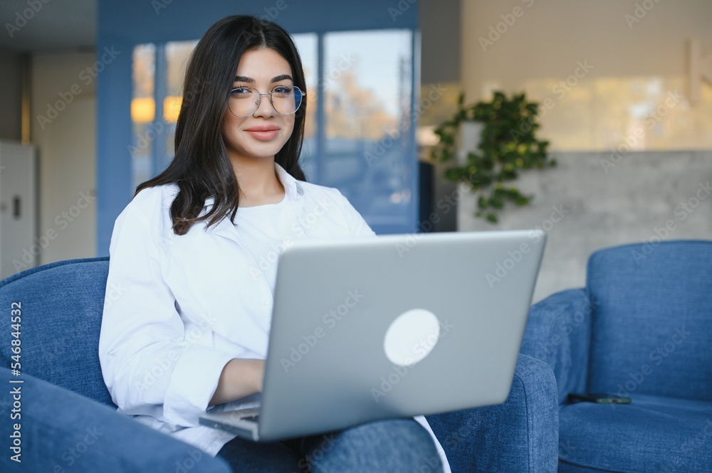 Beautiful Young Freelancer Woman Using Laptop Computer Sitting At Cafe Table. Happy Smiling Girl Working Online Or Studying And Learning While Using Notebook. Freelance Work, Business People Concept.