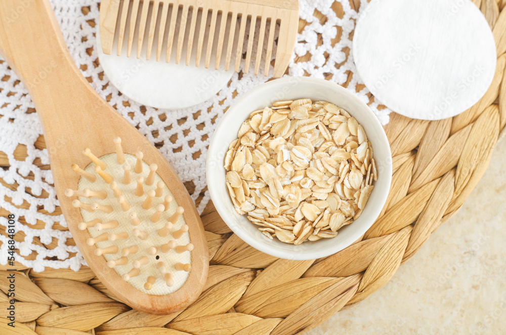 Rolled oats in a small white bowl and wooden hairbrush. Ingredient for preparing homemade face or hair mask. Natural beauty treatment and spa recipe. Top view, copy space.