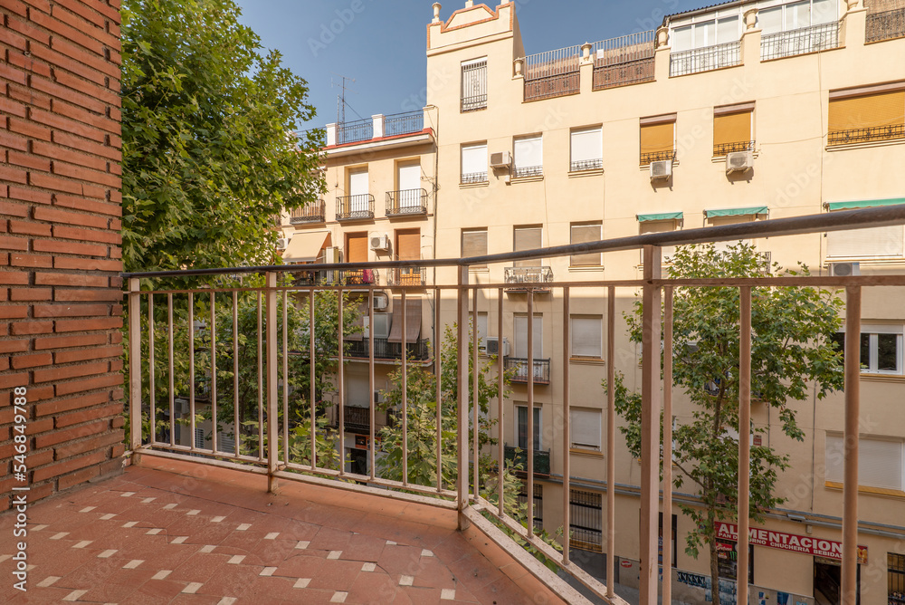 View of a street from a balcony with young trees, balconies with plants and skies with clouds and clear