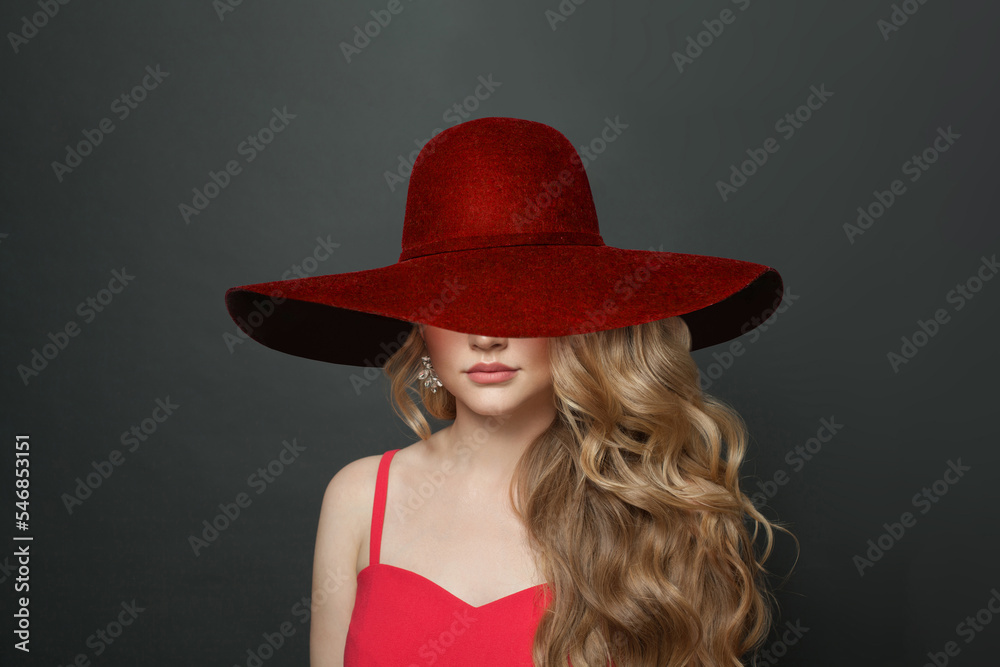 Blonde woman celebrity with makeup and long curly hairstyle in red wide broad brim hat on black background Blonde woman celebrity with makeup and long curly hairstyle in red wide broad brim hat on black background