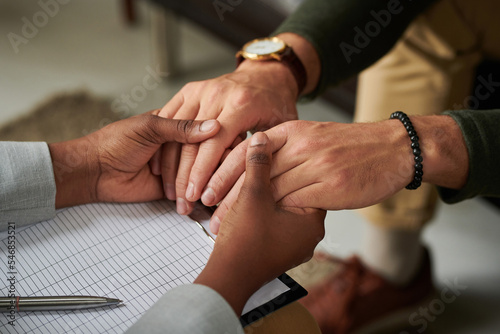 Close-up of psychotherapist holding hands with patient and supporting him at consultation