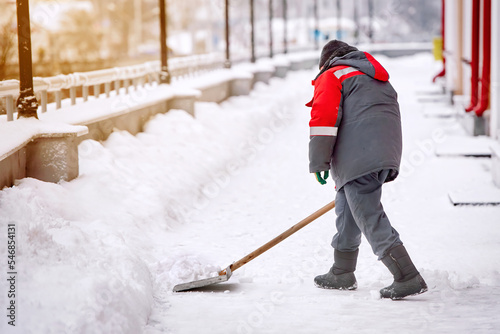 Man with shovel shoveling snow from sidewalk after heavy snowfall in winter season. Worker cleaning snow with shovel, snow removal work. Man clear snowy walkway.