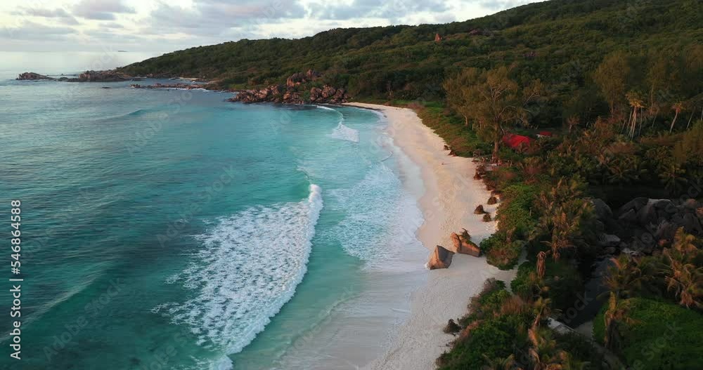 Drone flying past person standing on a rock. Captured on La Digue Island in the Seychelles at sunset.