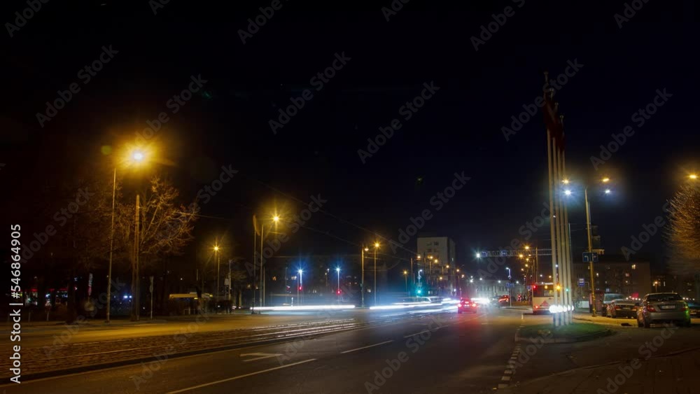 Timelapse of city rush hour traffic on the street of Liepaja, traffic light streaks, tram rails with fast moving trams, pedestrians waiting for the public transport, wide shot Timelapse of city rush hour traffic on the street of Liepaja, traffic light streaks, tram rails with fast moving trams, pedestrians waiting for the public transport, wide shot