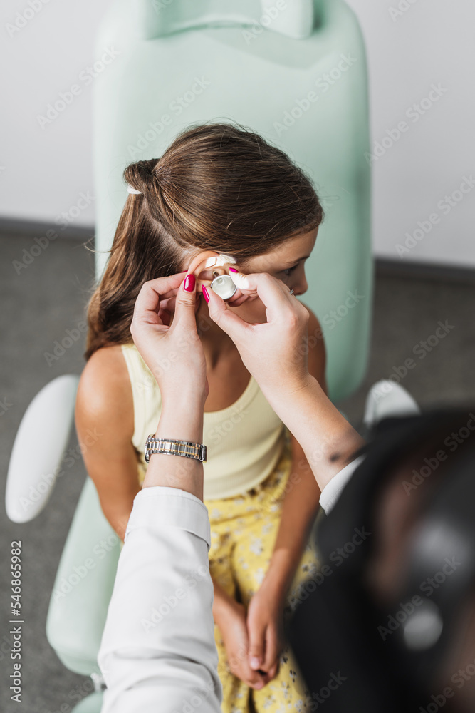 Female audiologist examining girl ear using otoscope in doctors office