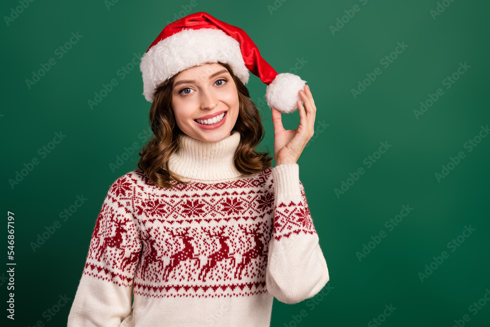Portrait of lovely attractive girl toothy smile hand touch hold newyear hat pompom ball isolated on green color background Portrait of lovely attractive girl toothy smile hand touch hold newyear hat pompom ball isolated on green color background
