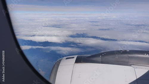 Airplane flight. Wing of an airplane flying above the clouds. View from the window of the plane. Airplane, Aircraft. Traveling by air. Aircraft's wing and land seen through the illuminator. 4K