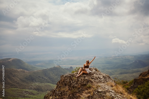Young woman freelancer traveler working online anywhere outdoors using laptop enjoying mountain peak view. Happy female downshifter in sunglasses holding computer in unusual workplace at summer