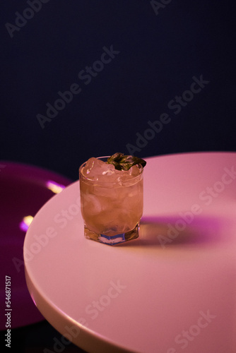 cocktail with alcohol with basil and ice in a low rocks glass on a white table
