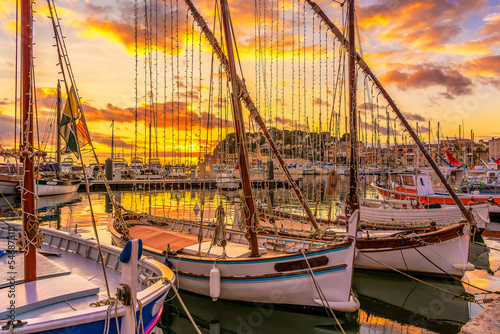 Scenic view of old fishing boats decorated with Christmas lights in the small port of Sanary sur Mer in south of France against dramatic golden winter